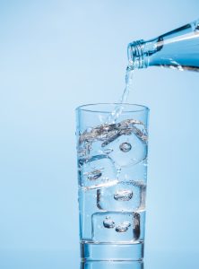 Crystal clear water being poured into a transparent glass with ice, creating refreshing ripples and bubbles. A perfect representation of hydration and purity